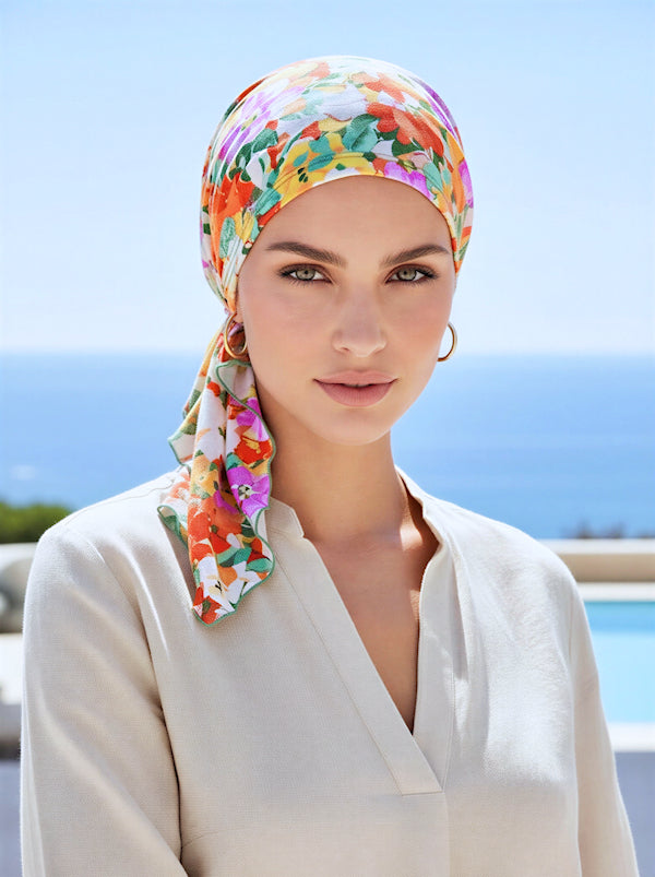 A woman wearing an orange and sage green floral patterned pre-tied head scarf.