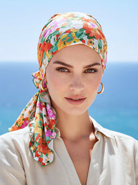 A woman wearing an orange and sage green floral patterned pre-tied head scarf.